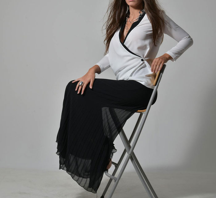 Woman sitting on a chair wearing a black skirt and white top, showing style without wearing a traditional dress for a wedding.