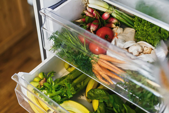 Open fridge drawers filled with fresh vegetables and fruits symbolizing parenting and family care.