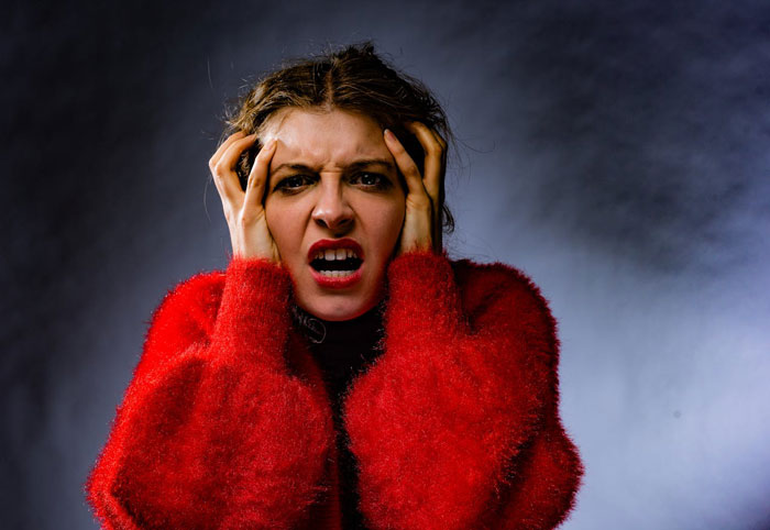 Woman goes berserk, frustrated and angry, holding her head while reacting to brother meddling with her parenting.