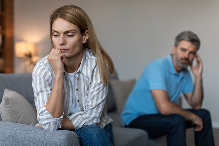 Worried woman sits on couch with partner in background after son is left without a ski pass amid salary tensions.