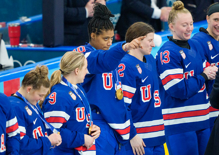 Team USA women&rsquo;s hockey stars in blue jerseys with gold medals, expressing unity and strength on the ice rink.