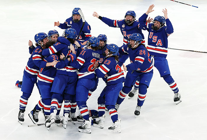 US Women's hockey players celebrating on ice wearing blue USA jerseys after a victorious game moment.