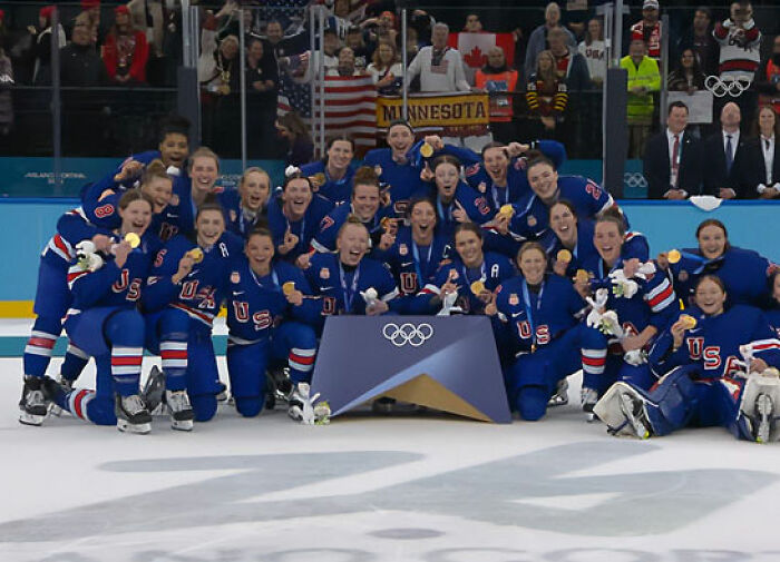 Team USA men's hockey team posing with gold medals on ice after winning at the Olympics with fans in the background. Team USA men's hockey team posing with gold medals on ice after winning at the Olympics with fans in the background.