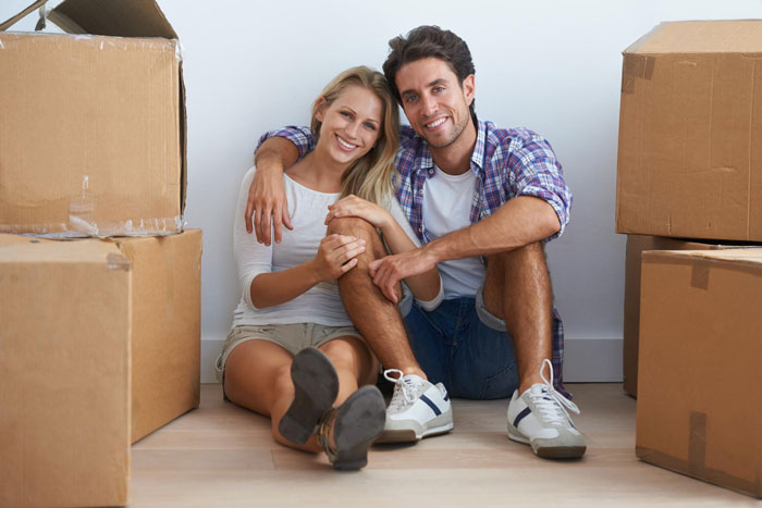 Young couple sitting on floor surrounded by moving boxes, representing woman judging coworker&rsquo;s life choices and morals.
