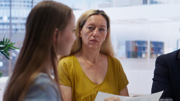 Woman in a yellow shirt judging coworker during a serious office discussion about life choices and morals.