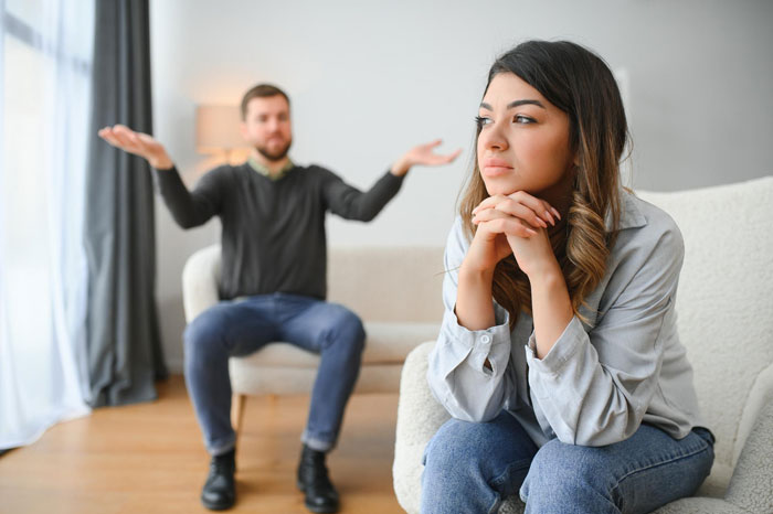 Woman looking stunned and thoughtful while her boyfriend gestures in frustration during a tense conversation about success.