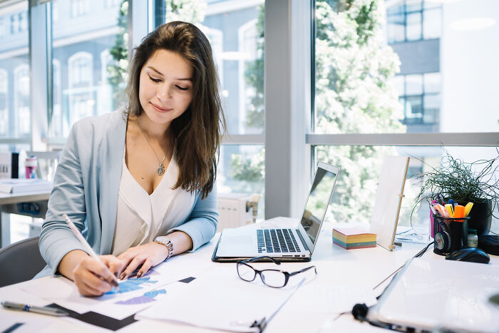 Young woman working at desk in modern office, focused on task amid displays of entitlement and patience challenges.