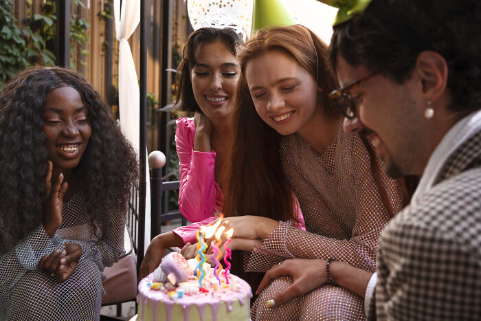 Group of friends smiling around a birthday cake with lit candles, capturing moments of entitlement and celebration patience.