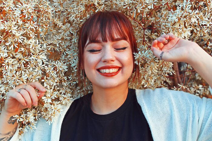 Smiling woman with red hair posing joyfully among white flowering branches in a bright outdoor setting for would you still do it poll.