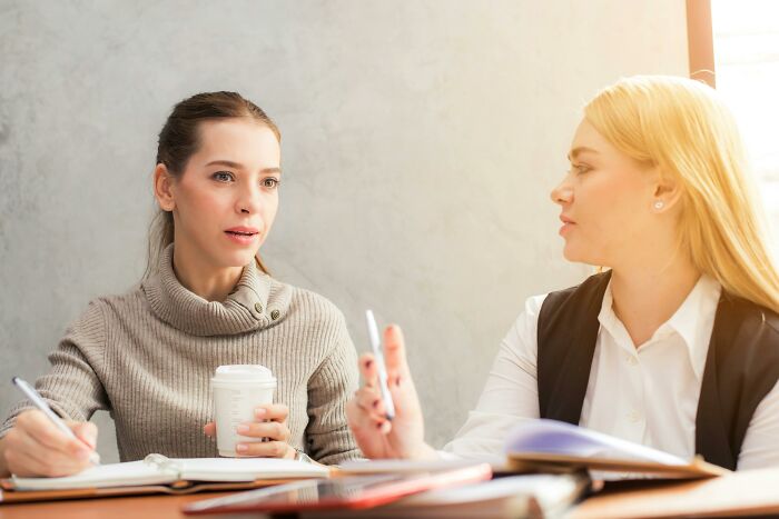 Two women having a serious discussion over notes and coffee during a would you still do it poll session.