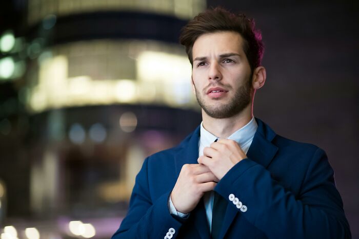 Young man adjusting his tie outdoors at night, appearing thoughtful and focused in the would you still do it poll context.
