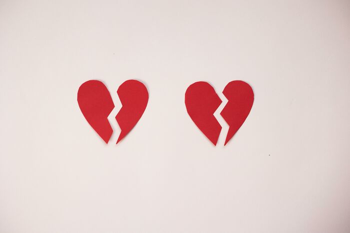 Two red broken paper hearts placed on a white surface, symbolizing love and emotions for Would You Still Do It Poll.