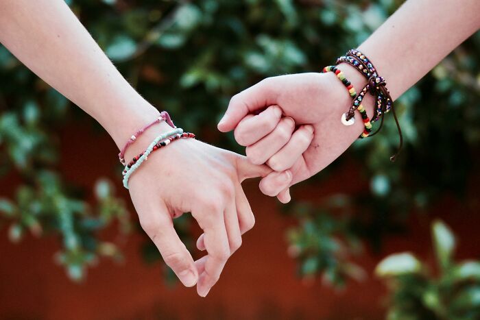 Two hands linking pinkies wearing colorful bracelets, symbolizing connection for would you still do it poll concept.