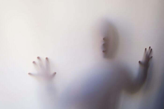 Blurred figure pressing hands and face against frosted glass, illustrating suspense for Would You Still Do It poll.