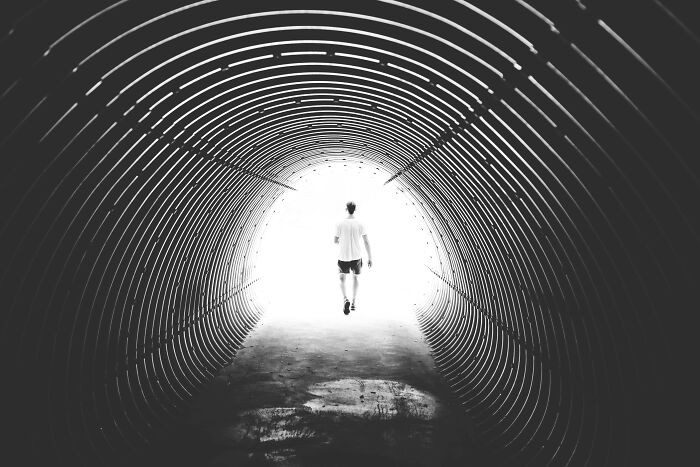 Person walking toward bright light at the end of a corrugated metal tunnel, concept for would you still do it poll.
