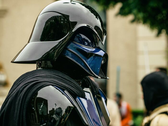Cosplay character in black shiny armor and helmet at an outdoor event, captured for Would You Still Do It poll.