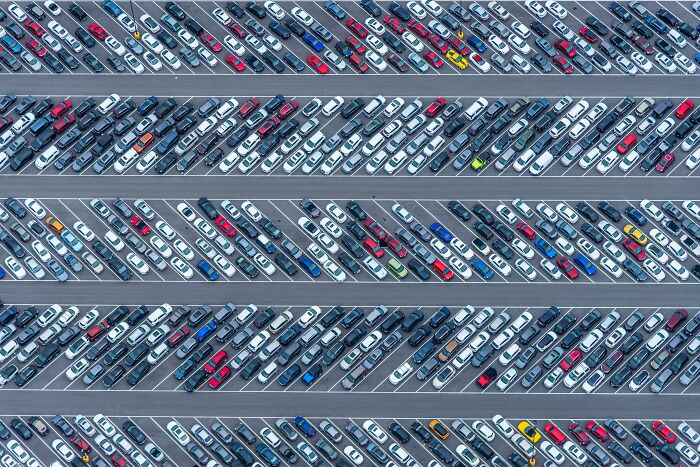Aerial view of a large parking lot filled with rows of cars in various colors, illustrating a would you still do it poll.