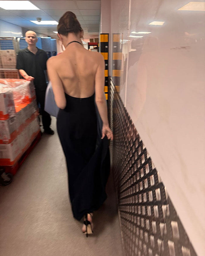 Emma Stone walking in a black backless dress, showing a cadaverous appearance backstage at the 2026 BAFTAs event.