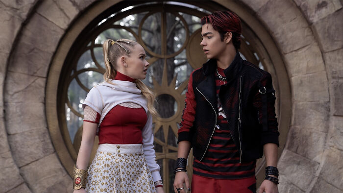 Two young actors in costume standing before a large circular stone window scene from Zombies 5 release date, cast, and plot.