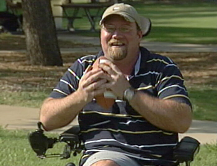 Man in a wheelchair smiling and holding an object outdoors, illustrating disturbing real life nightmare facts and images.