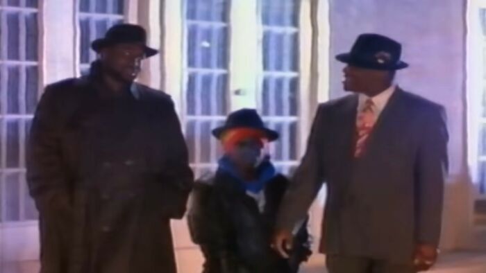 Three people dressed in vintage coats and hats standing together, illustrating weird and unhinged family traditions.