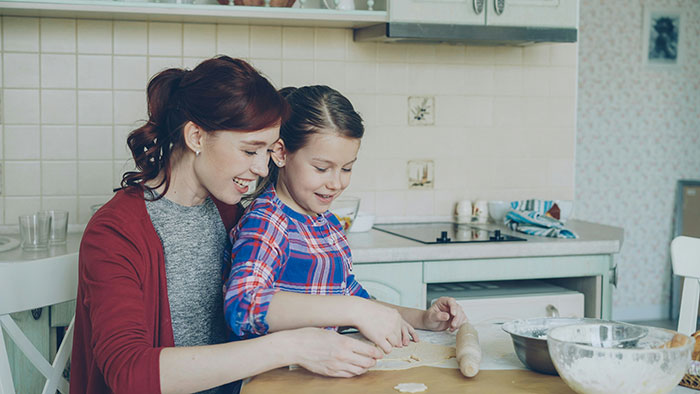 Mother and daughter baking together in a kitchen, with a rolling pin and dough on the table, DNA testing tension unseen.
