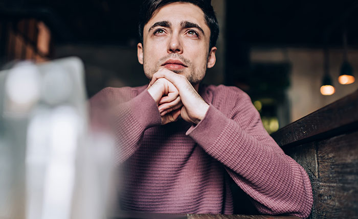Man in a purple sweater sitting thoughtfully at a wooden table, reflecting on adopting wife's kids after spying.