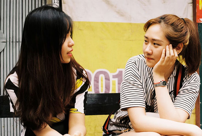 Two young women sitting and talking intensely in an urban setting, reflecting a story about refusing to adopt wife's kids.