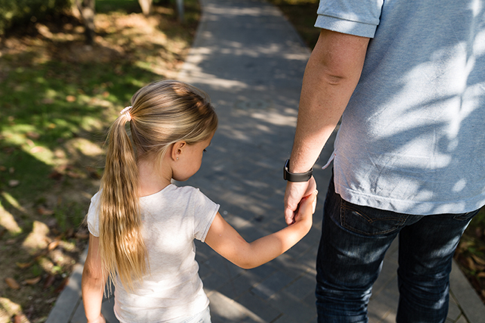 Single man holding hands with young girl outdoors, symbolizing life changes after call from child services. Single man holding hands with young girl outdoors, symbolizing life changes after call from child services.