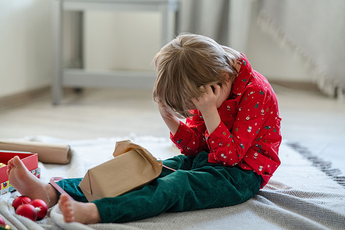 Sad young boy sitting on floor holding head, depicting emotional distress and family alienation over niblings being brainwashed.