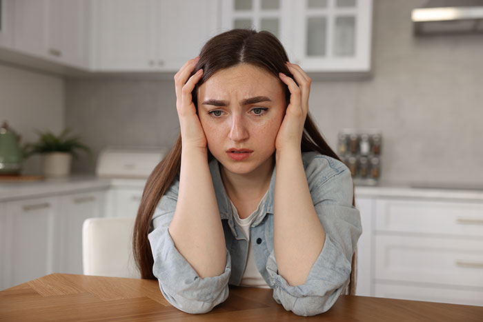 Teen vegan looking upset while sitting at kitchen table after being made to cook meat to avoid food waste.