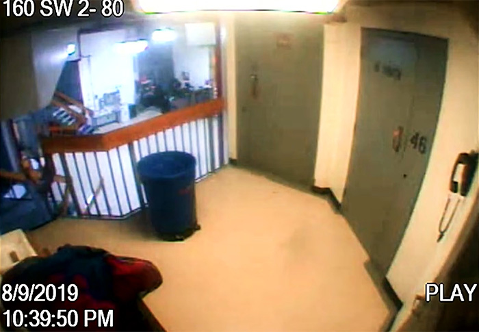 Security camera footage showing prison hallway with cells and timestamp related to Epstein prison guard activity.