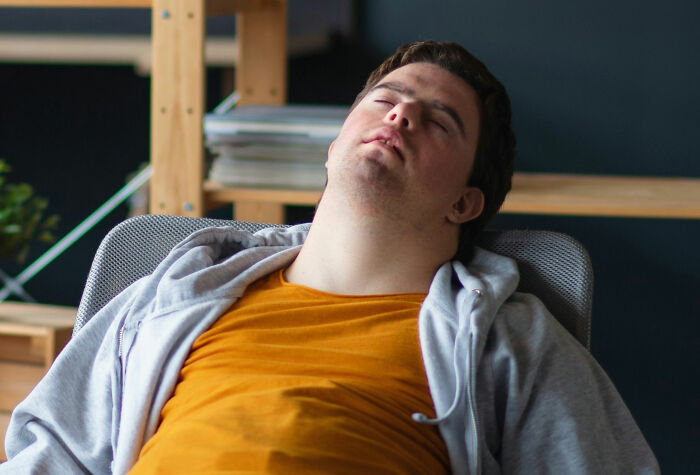 Young man asleep in a chair wearing casual clothes, illustrating exhaustion during weird family traditions or unusual habits.