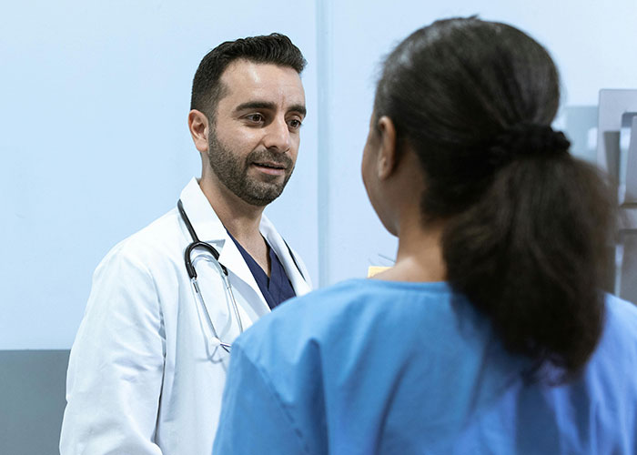 Male doctor with stethoscope talking to a patient in blue scrubs, revealing medical secrets in a clinical setting.