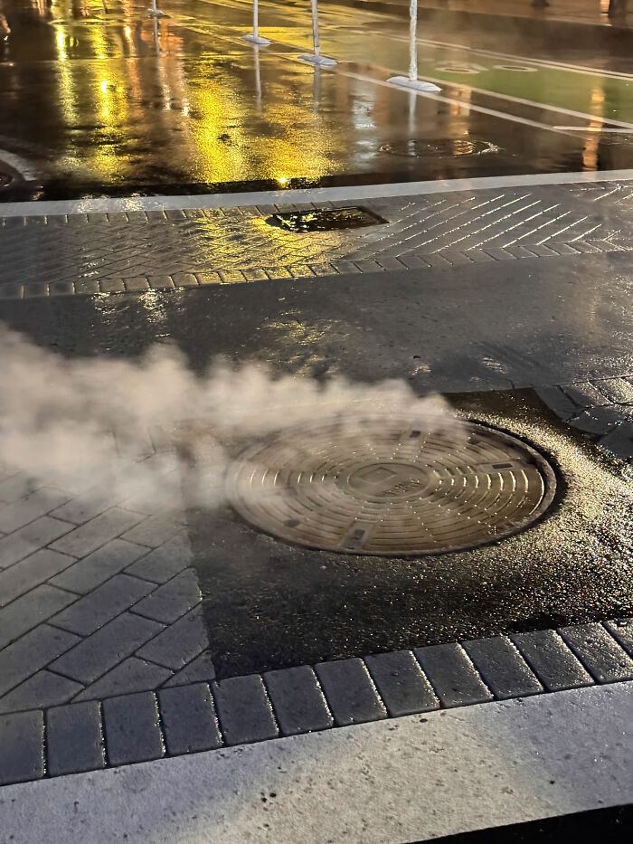 Steam rising from an urban manhole cover on a wet street at night, showing a real American city scene.