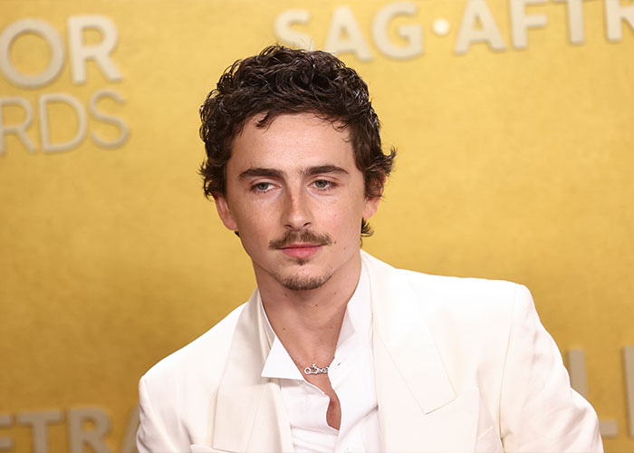 Timoth&eacute;e Chalamet at a SAG Awards event wearing a white suit with a serious expression discussing Oscar chances.