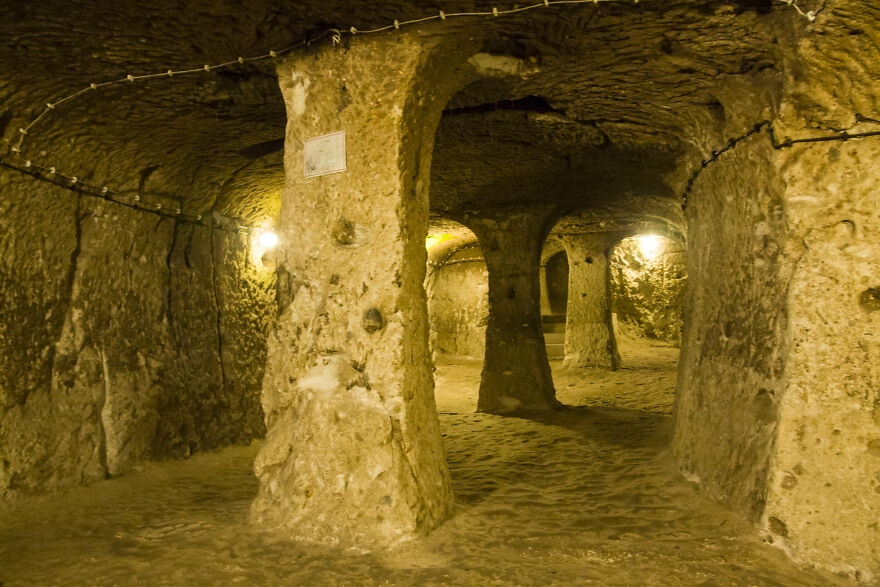 Underground city interior with stone pillars and warm lighting showcasing ancient tunnels carved into rock walls.