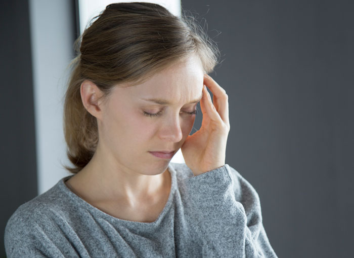 Woman in gray sweater touching her temple, looking distressed and reflecting on losing a friend to a tumour.