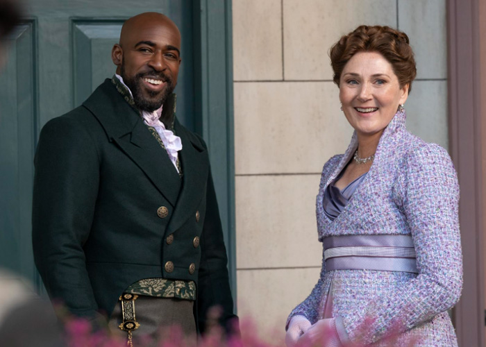Actors in Bridgerton period costumes smiling on set, highlighting Ruth Gemmell's emotional experience filming intimate scenes.