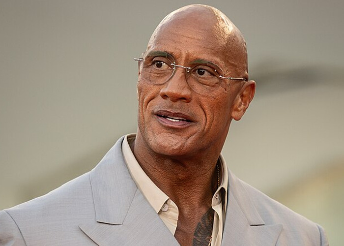 Bald celebrity wearing glasses and a beige suit, illustrating people met celebrities who turned out to be raging jerks.