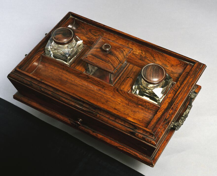 Antique wooden inkstand with glass inkwells and a central covered compartment, a curious object with dazzling origins.