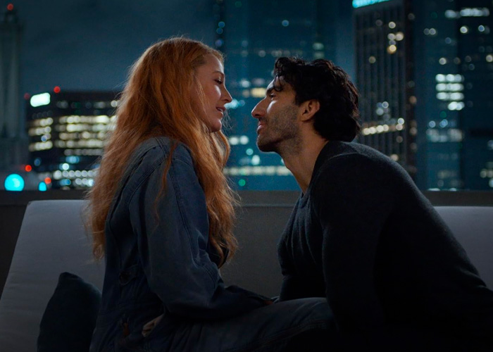 Couple sitting face to face on a rooftop at night with city lights, hinting at Justin Baldoni’s legal battle with Blake Lively.