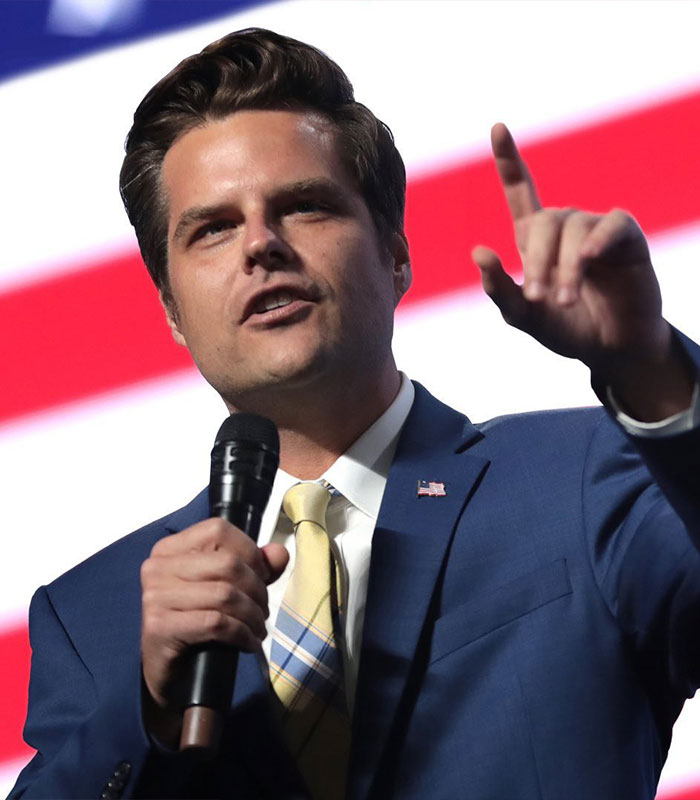 Man in a blue suit speaking into a microphone, related to Reacher star Alan Ritchson under investigation after altercation.