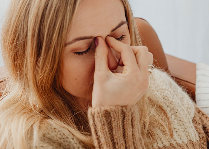 Young woman in a cozy sweater holding her face in pain after an injury, illustrating unserious reasons for ER visits.