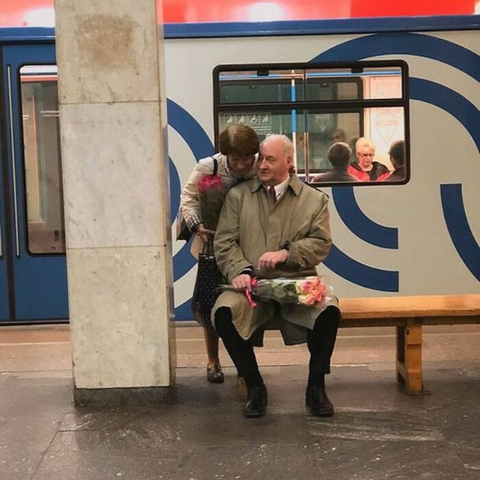 Elderly couple sharing a tender moment at a subway station with flowers, representing uplifting posts about kindness.