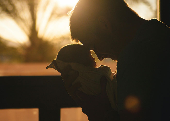 Man holding baby close to his face, capturing a tender and emotional moment of love and connection at sunset.