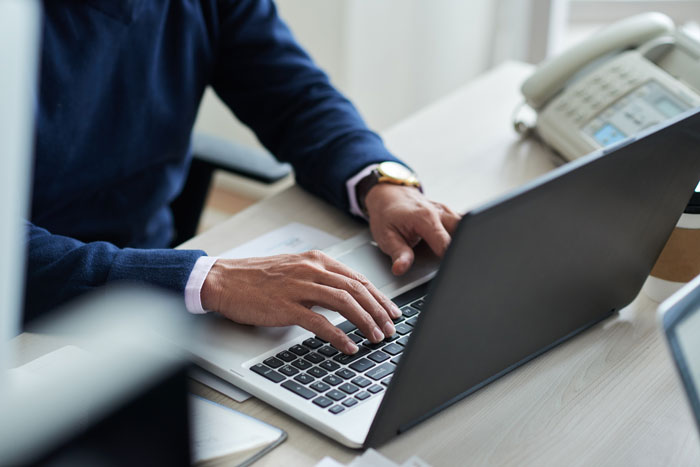 Person in a blue sweater typing on a laptop at a desk, symbolizing corporate secrets exposed to customers.