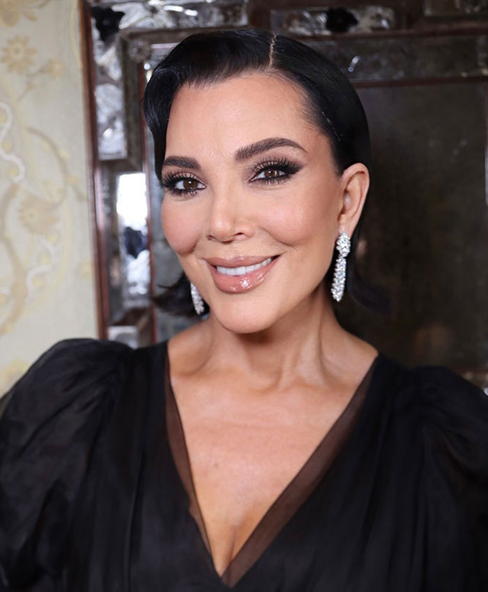 Woman smiling after cosmetic procedure, wearing black dress and sparkling earrings in an elegant indoor setting