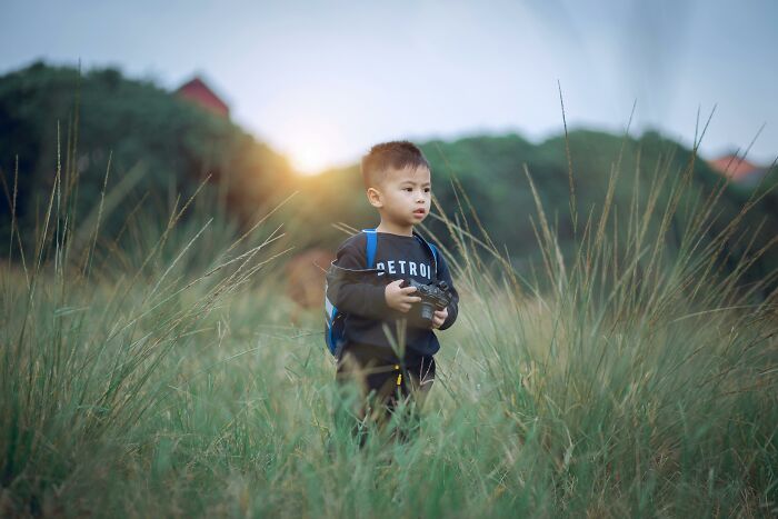 Young boy standing in tall grass holding a camera, representing themes of peer pressure.