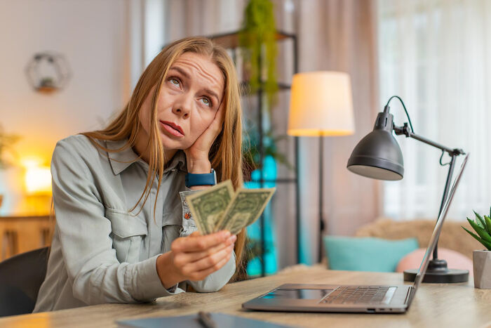 Woman looking stressed while holding money in hand at a desk, illustrating tough reasons for staying in a relationship.